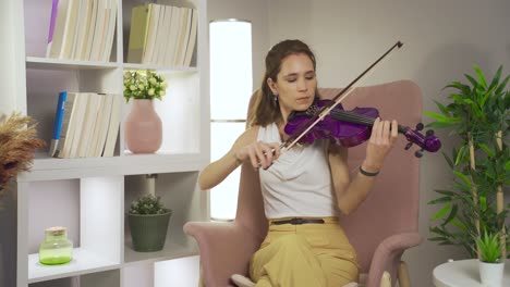 Talented-musician-woman-playing-violin-sitting-on-sofa-at-home.